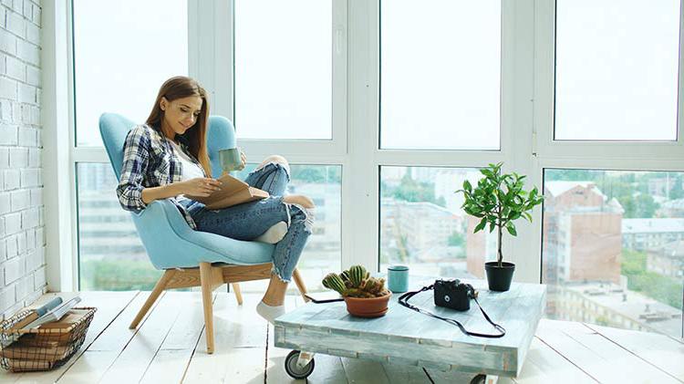 Woman reading in chair in front of window, looking happy due to 购买 a condo.