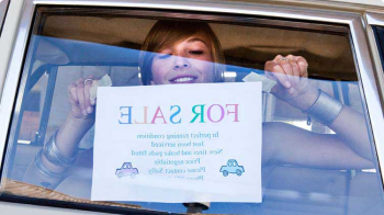 一位微笑的年轻女士在她的车窗上贴着“出售”的牌子.
